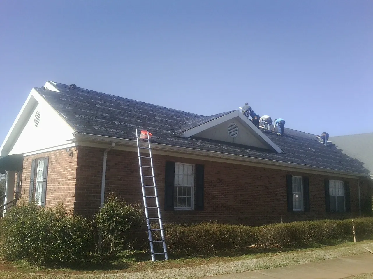 Crew tearing shingles off a brick ranch roof with a ladder set — Metal Roof Repair work by our crew in Wahkiacus