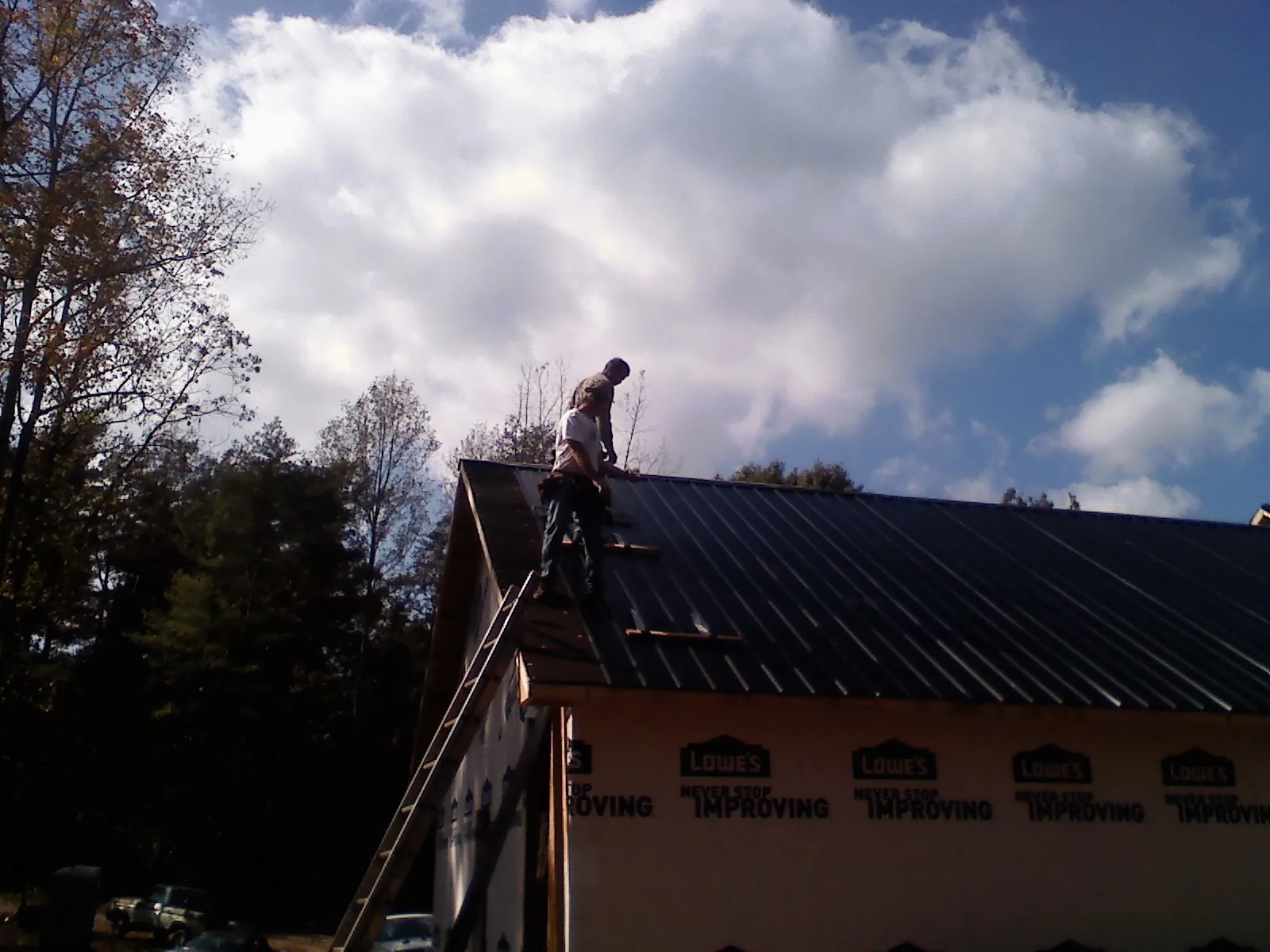 Roofer fastening dark metal panels high against a cloudy sky, from a Roof Inspection job in Wahkiacus