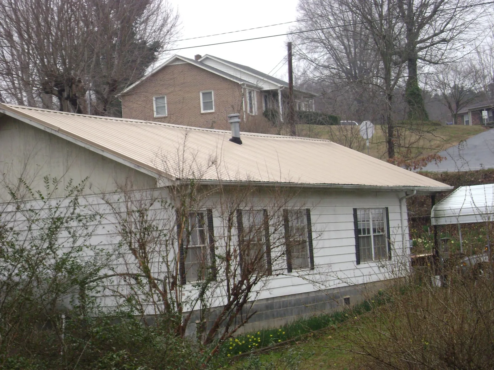 Tan metal roof on a white sided house set into a hillside — Commercial Roofing by Roofing Brothers in Wahkiacus